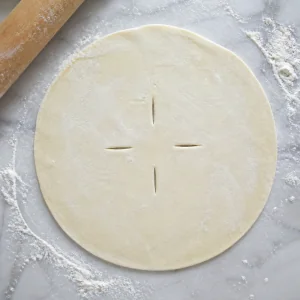 Round puff pastry sheet with steam vents on a floured surface