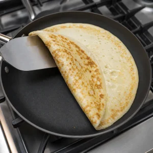Niederlaendischer Pfannkuchen mit breitem Spatel gewendet und goldbraun gefleckt