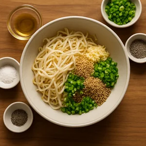 A bowl holds sprouts with garlic, sesame oil, sesame seeds, and chopped green onion.