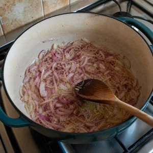 Cebola roxa fatiada finamente refogando em oleo numa panela pesada