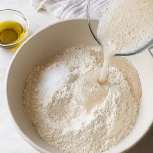 Schaeumende Hefemischung und Olivenoel werden zu Brotmehl und Meersalz gegossen