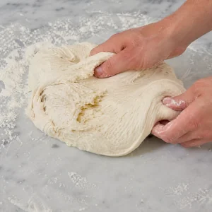 Pizza-bianca-Teig wird auf leicht bemehlter Flaeche elastisch geknetet