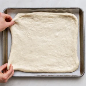 Pizza-bianca-Teig auf einem mit Backpapier ausgelegten Blech ausgebreitet