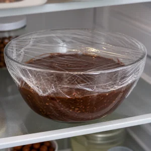 Chocolate hazelnut ganache covered with plastic wrap chilling in the refrigerator.