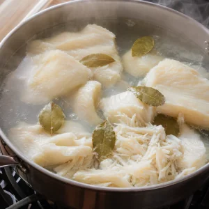 Poached cod flaking beside bay leaves