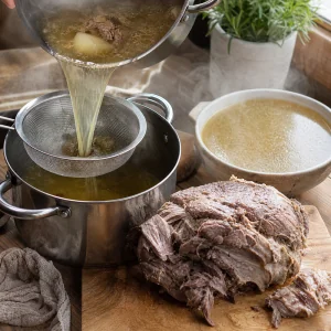 Agneau braise au repos pendant que le bouillon chaud est filtre dans une marmite propre