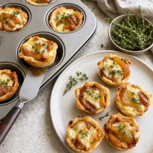 Finished Brie-and-Apple Tarte Tatin Bites garnished with fresh thyme and lifted from a muffin tin to serve warm