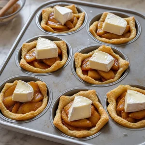 Pastry cups filled with caramelized apples and topped with brie pieces before baking