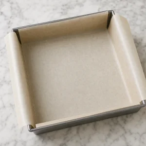 Parchment-lined square baking pan ready for cannoli squares