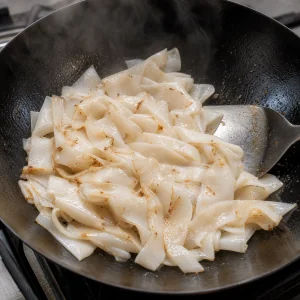 Wide rice noodles spread in a wok