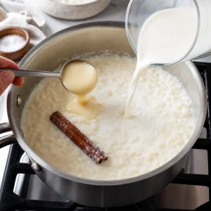 Milk, condensed milk, and a cinnamon stick added to the saucepan of rice.