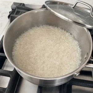 Rice simmering with water in a saucepan until the liquid is mostly absorbed.