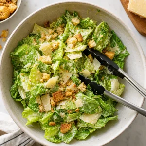 Chopped romaine tossed with Caesar dressing, Parmesan cheese, and crushed croutons in a bowl.