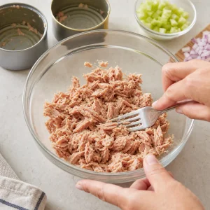 Drained canned tuna flaked with a fork in a mixing bowl