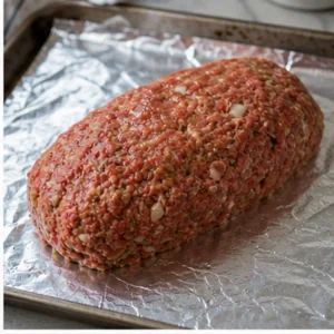 Polpettone crudo formato in un cilindro ordinato su una teglia rivestita di alluminio