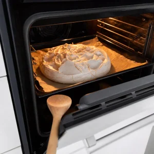 Baked pavlova cooling slowly in the turned-off oven with the door slightly ajar.