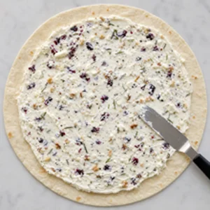 Cranberry feta cream cheese mixture spread evenly over a flour tortilla with a clean edge