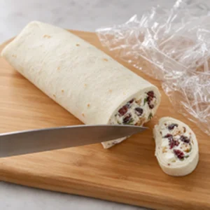 Unwrapped chilled tortilla roll trimmed at the end with a sharp knife on a cutting board