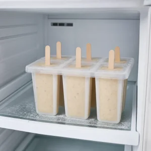 Filled banana ice pop molds with wooden sticks chilling in the freezer