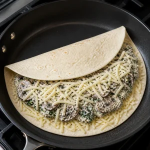 Tortilla filled with creamy mushroom spinach filling and shredded cheese.