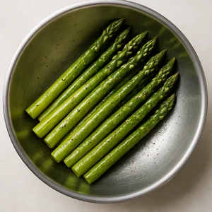 Asparagus spears in a bowl, evenly coated with oil and seasonings.
