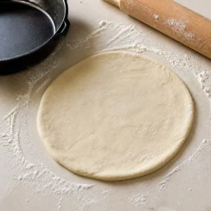 Disco pequeño de masa de pizza estirado sobre una superficie enharinada