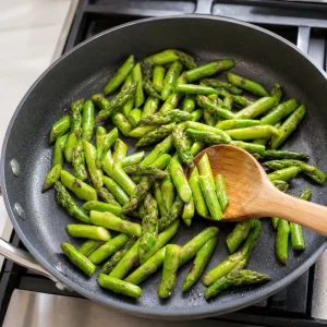 Pedaços de aspargo salteando na frigideira até ficarem verde-vivos e macios, porém crocantes.