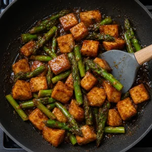 Tofu e aspargos misturados em um glacê espesso e brilhante de gengibre e soja.