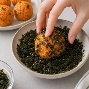 Ein Kimchi-Reisbällchen wird in zerbröselten gerösteten Algen gewälzt.