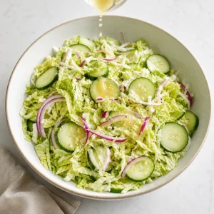 Leichtes Dressing wird ueber Chinakohl-, Gurken- und rote-Zwiebel-Salat getraeufelt.
