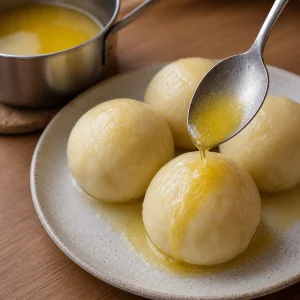 Melted butter being spooned over warm fruit dumplings