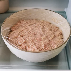 Covered bowl of frikadeller mixture resting in the refrigerator
