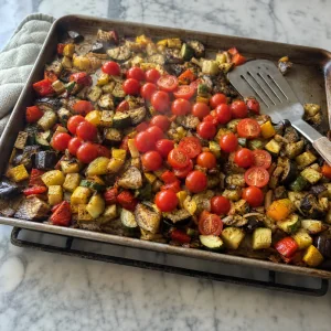 Teilweise geröstetes Gemüse mit frischen Cherrytomaten auf dem heißen Blech vermengt.