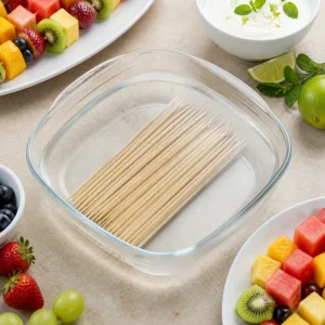 Bamboo skewers soaking in cold water with fruit nearby