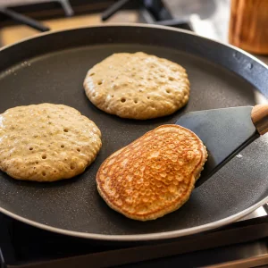 Banana oat pancakes bubbling on a skillet as one is flipped golden