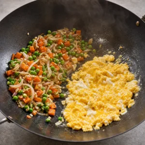 Soft scrambled eggs beside sauteed vegetables in a wok