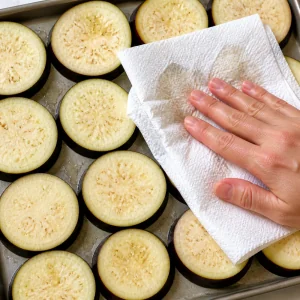 Eggplant slices being patted dry with paper towels