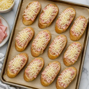 Shredded cheese sprinkled over ham-topped garlic toasts