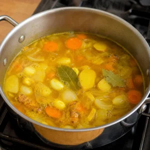 Caldo dorado de jengibre y cúrcuma hirviendo suavemente con raíces, zanahorias, cebolla y laurel