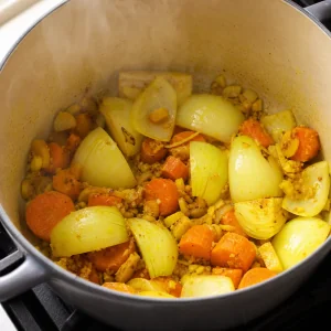 Cebolla en cuartos ablandándose con jengibre, cúrcuma, ajo y zanahorias en una olla