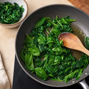 Spinach wilting in a skillet with a wooden spoon