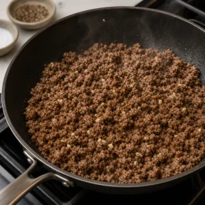 Browned ground beef cooking with garlic in a skillet.