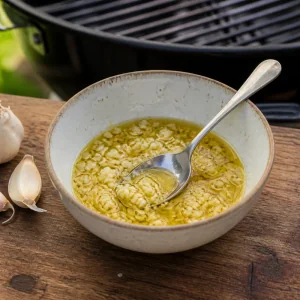 Minced garlic stirred into olive oil beside a grill