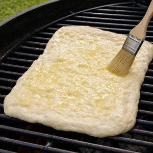 Pizza dough on grill grates brushed with garlic oil