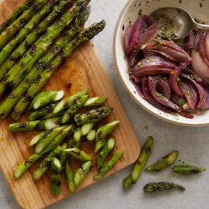Grilled asparagus cut into angled pieces with onions nearby