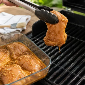 Marinated chicken draining beside hot oiled grill grates