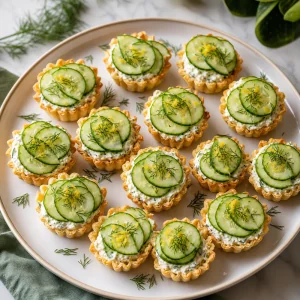 Finished herbed cream cheese cucumber tarts arranged on a serving platter.
