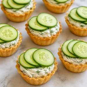 Thin cucumber slices arranged slightly overlapping on filled tartlets.