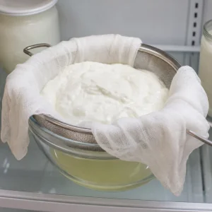 Joghurt tropft durch ein Kaesetuch in einem Sieb fuer griechischen Stil