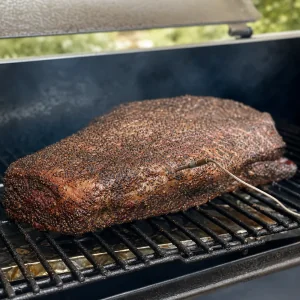 Pepper crusted brisket smoking low and slow on a smoker grate